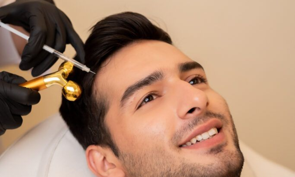 A man smiling while receiving a hair regrowth treatment, which appears to involve microneedling and an injection to the scalp at an aesthetic clinic.