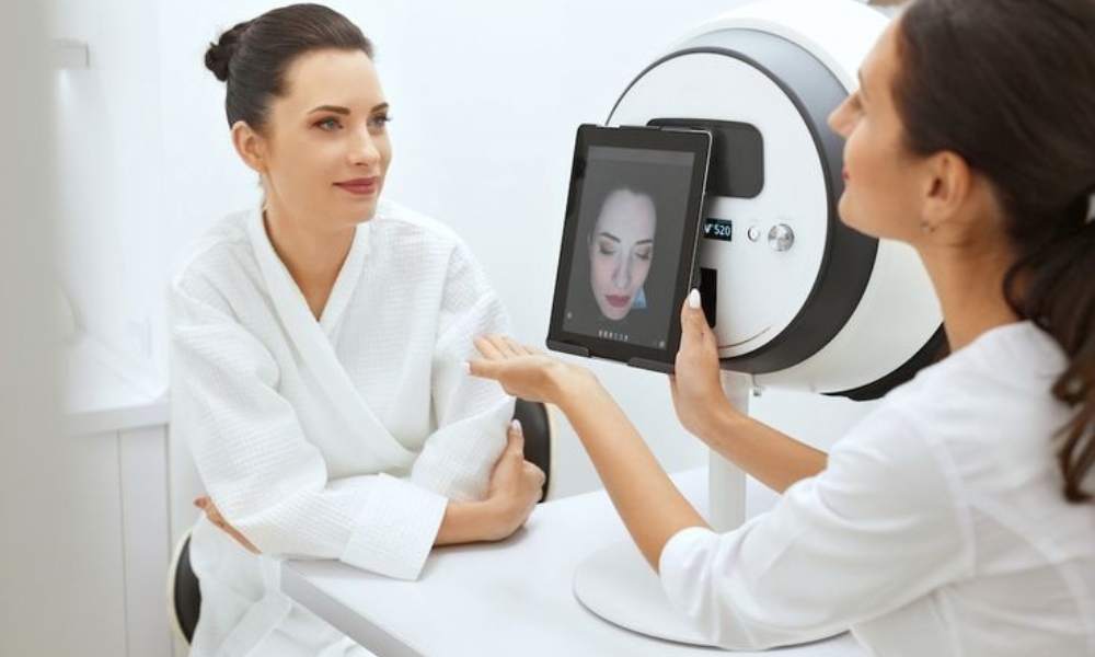 Two women, likely a clinician and a client, using a skin analysis device during a consultation at an aesthetic clinic.