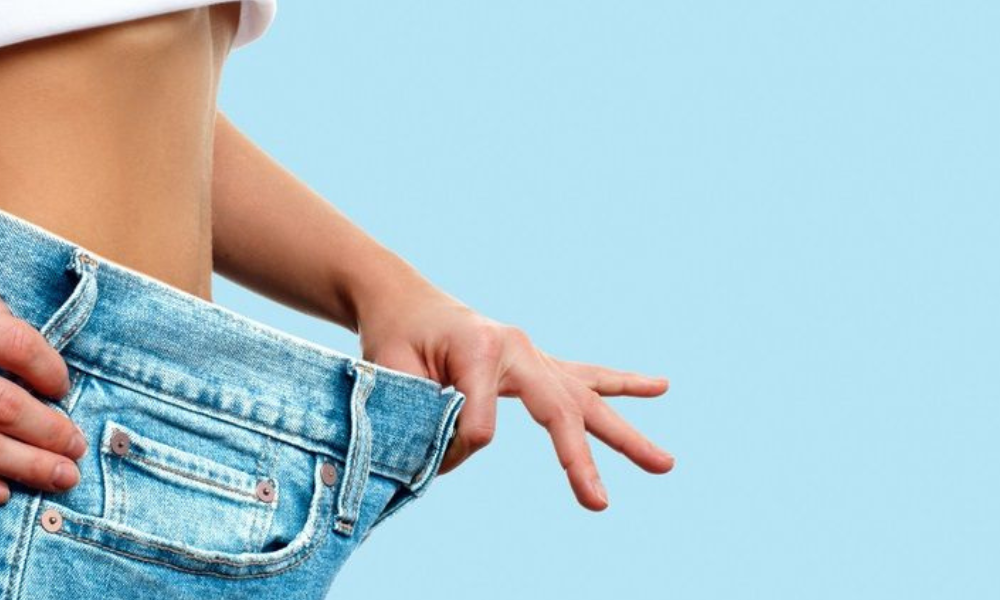 Person pulling loose jeans away from their waist, showing weight loss.