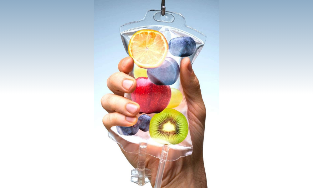 Hand holding a clear IV drip bag filled with colorful fruit slices.